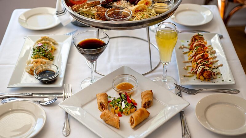 Multiple plated appetizers with wine and a orange cocktail
